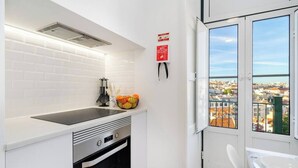 A modern kitchen with a black stove, white cabinets, and a window overlooking a cityscape.