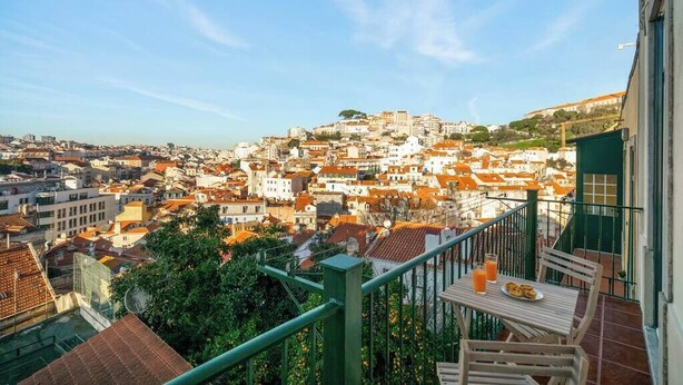 A balcony with a table, chairs, and a view of a cityscape with buildings and a hill.