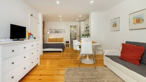 Quarto moderno e bem iluminado, com uma cama, um sofá branco, uma mesa de jantar e uma TV em um aparador.