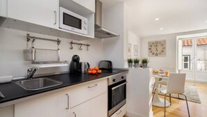 Uma cozinha moderna com micro-ondas, forno e pia. Há uma área de refeições com mesa e cadeiras.