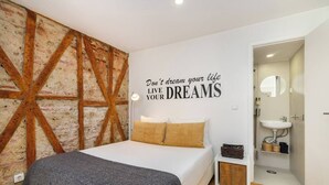 Quarto com cama, frase motivacional na parede, piso de madeira e banheiro visível.