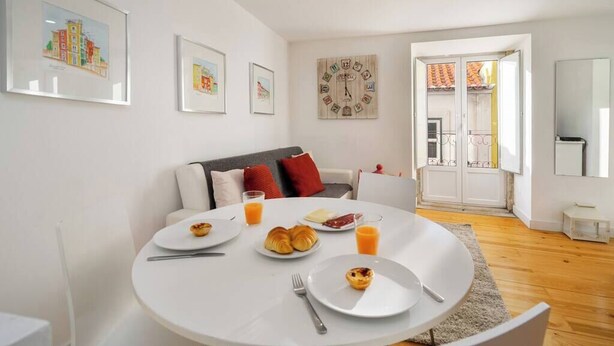 Uma sala de estar moderna com uma mesa de jantar redonda posta para o café da manhã, um sofá com almofadas e um relógio de parede grande.