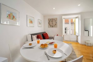 A modern living room with a round dining table set for breakfast, a sofa with cushions, and a large wall clock. - Martim Moniz Central Studio | Premium Location (Lisboa)