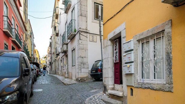 A narrow cobblestone street lined with colorful buildings, a parked car, and a utility box. - Paz 2 | Tram28 | Wi-Fi | AC | Bairro Alto (Lisboa)