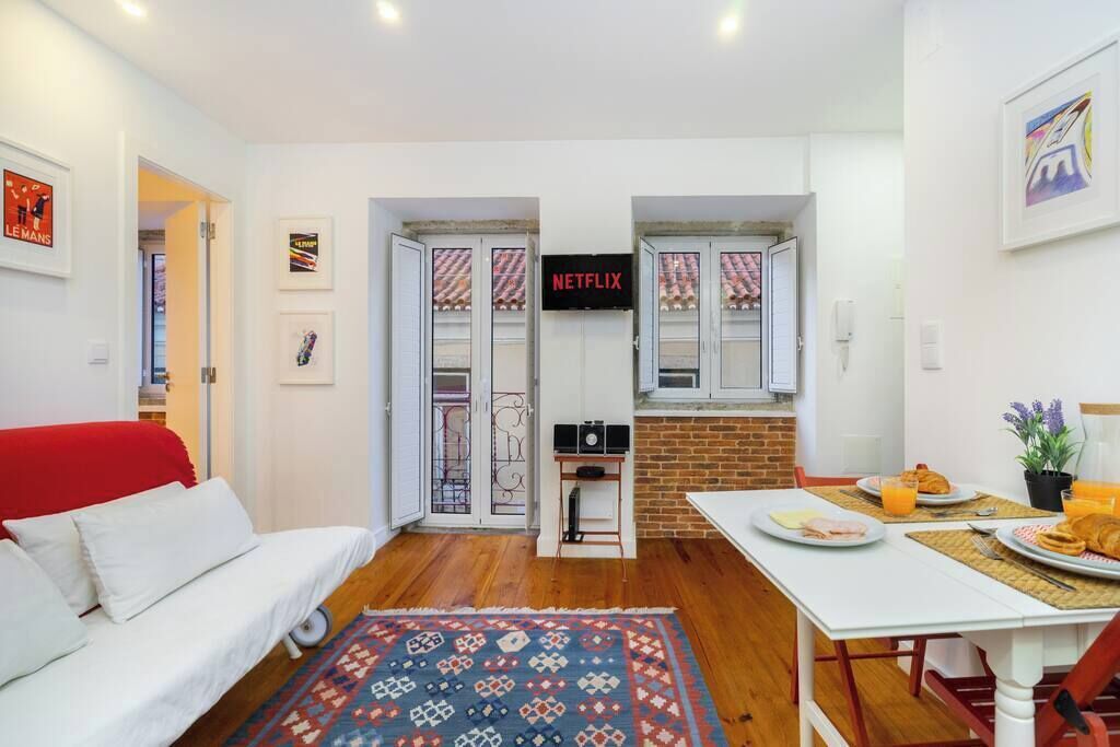 A compact living space with a sofa, a dining table with breakfast, a TV, and a patterned rug.