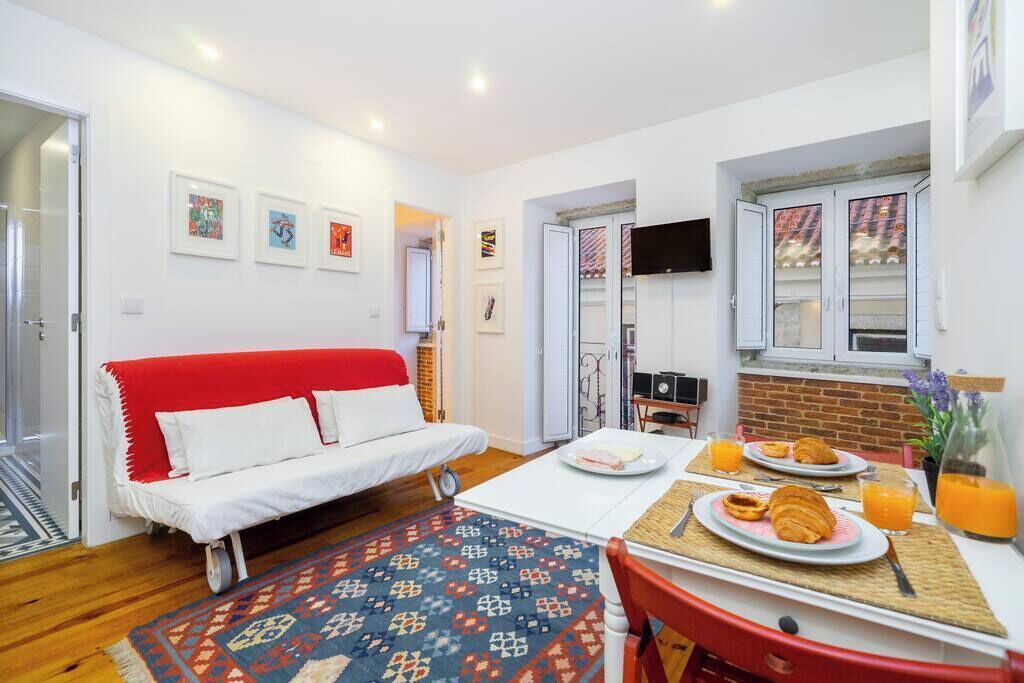 A compact living space with a red sofa, a dining table with breakfast, and a TV mounted on the wall.