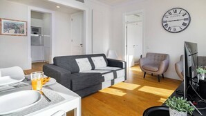 Una sala de estar moderna con un sofá gris, una mesa de comedor con platos y vasos, un sillón gris y un gran reloj de pared.