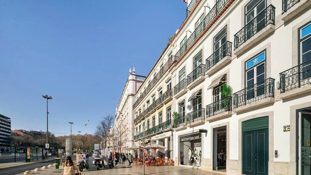 Calle con edificios, un peatón y mesas al aire libre.