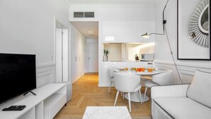 Ein modernes Wohnzimmer mit Flachbildfernseher, einem weißen Sofa, einem Marmor-Couchtisch und einem Essbereich mit weißem Tisch und Stühlen.