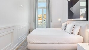 Ein Schlafzimmer mit einem großen Bett, Blick auf Gebäude durch ein Fenster und einem gerahmten Kunstwerk an der Wand.