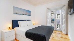Ein Schlafzimmer mit Bett, Nachttischen, einem Gemälde und Blick durch eine offene Tür.