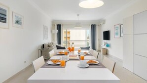 A modern dining area with a white table set for breakfast, including plates of food and glasses of orange juice. - Family Holidays w/ S-Pool | AC | Elevator | Garage (Quarteira)