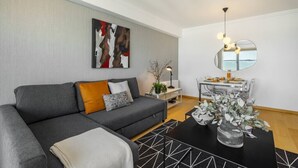 Ein modernes Wohnzimmer mit einem grauen Sofa, einem schwarzen Couchtisch und einem Essbereich mit einem Tischchen mit Spiegel.