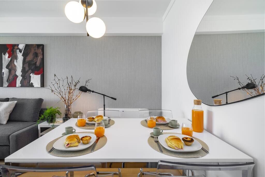 A modern dining area with a white table set for breakfast, including croissants and orange juice.