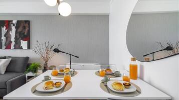 A modern dining area with a white table set for breakfast, including croissants and orange juice.