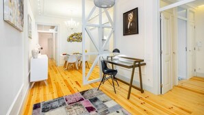 Ein modernes Interieur mit Holzboden, einem weißen Schreibtisch mit Stuhl, einer Pendelleuchte und einem gerahmten Bild an der Wand.