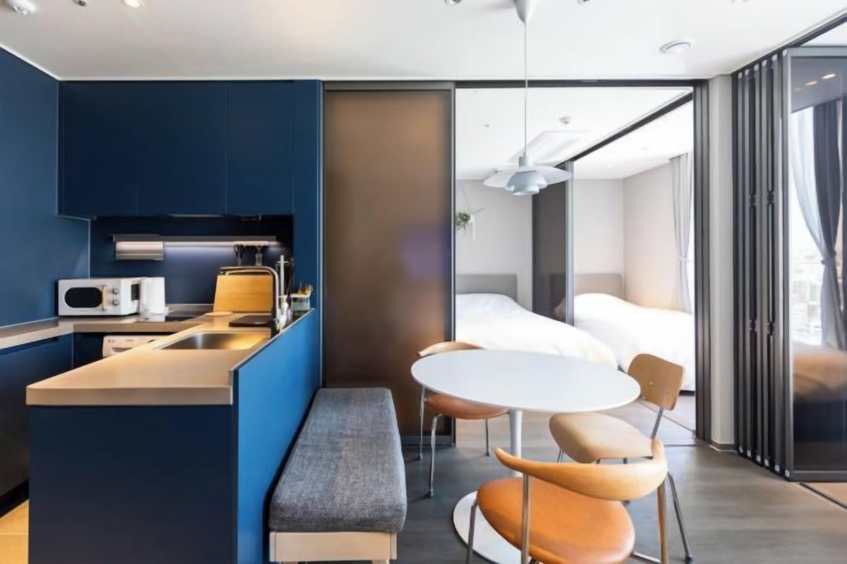 A modern hotel room with a kitchenette, a dining area, and a bed.