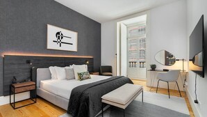 A modern bedroom with a large bed, bedside tables, a bench, a desk, and a TV.