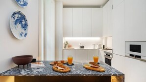 A modern kitchen with white cabinets, a marble countertop, and a breakfast setup with croissants and orange juice.