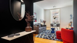 A modern living room with a sofa, a coffee table, and a red armchair. There is a dining area with a table and chairs, and a large window providing a view of the outside.