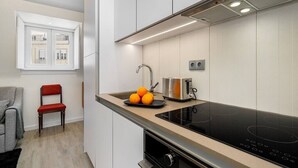 Eine moderne Küche mit Einbauherd, Spüle und Toaster. Über der Spüle befindet sich ein Fenster und im angrenzenden Raum ein Stuhl.