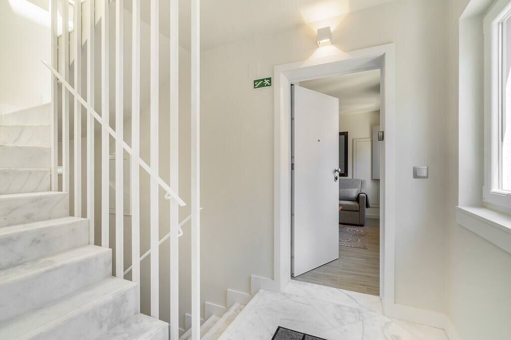 Un escalier avec des rampes blanches menant à une pièce où se trouvent un lit et une fenêtre.