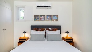 Een slaapkamer met een bed, twee nachtkastjes, een raam, een airconditioner en vier ingelijste foto's aan de muur.