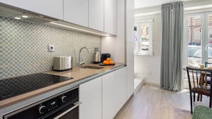 Een moderne keuken met een inbouwoven, een spoelbak en een broodrooster. Een eethoek met een tafel en stoelen is zichtbaar door een open deur.