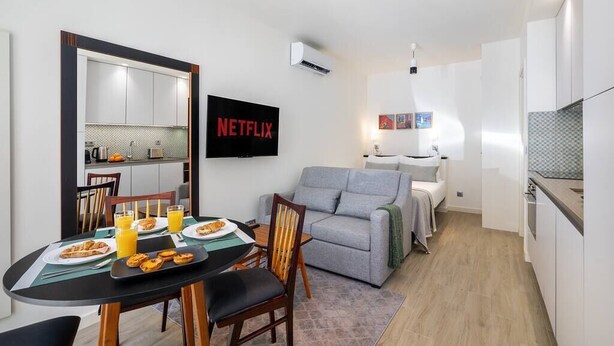 A compact living space with a dining area, kitchenette, and a gray sofa. - Lisbon Prime Aparts - Anjos (Lisboa)