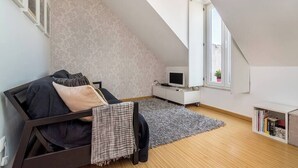 A loft bedroom with a sloped ceiling, a bed with pillows, a TV, a bookshelf, and a window with a plant. - Cozy Apartment in Lisbon’s Prime Area (Lisboa)