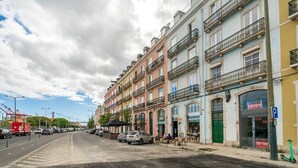 Rua com edifícios altos, carros estacionados e uma área para pedestres.