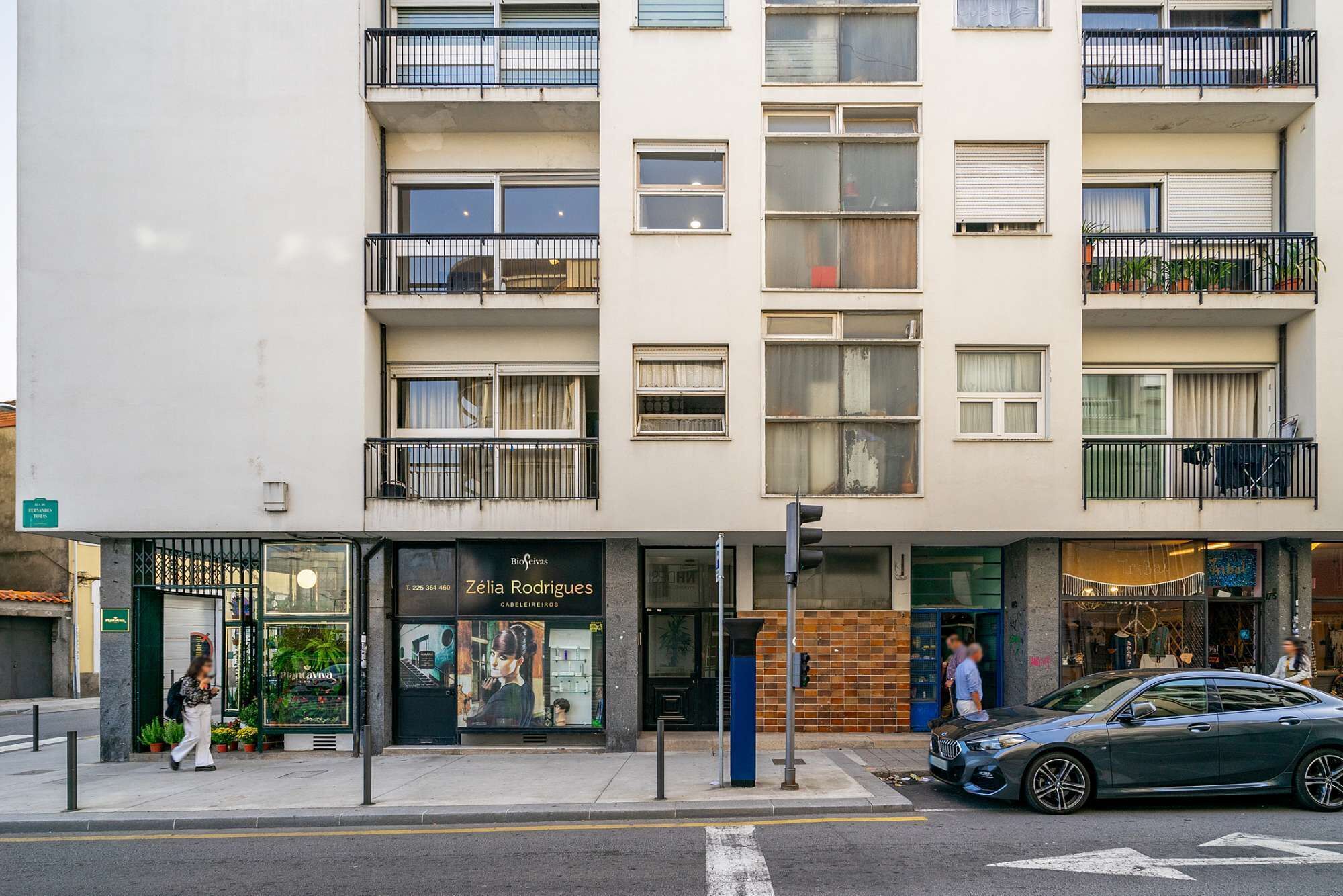 A multi-story building with balconies, a storefront with a sign reading "Zélia Rodrigues GARELIEROS," and a parked car on the street.