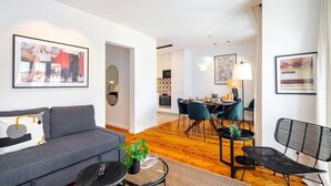 Ein modernes Wohnzimmer mit grauem Sofa, Couchtisch und einem Essbereich mit Stühlen und Tisch.