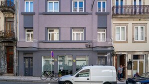 Un edificio de varios pisos con un espacio comercial en la planta baja, una camioneta blanca estacionada frente a él y una bicicleta apoyada contra la pared.