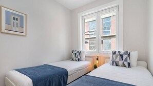 Habitación de hotel con dos camas, una ventana con vista a edificios y un cuadro en la pared.