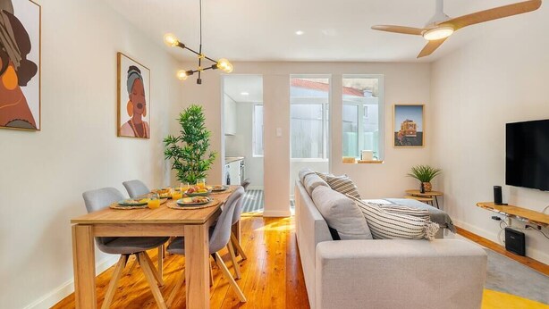 Una sala de estar moderna con un sofá, una mesa de comedor con sillas, un televisor y un ventilador de techo.