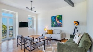 Un vaste espace de vie doté d’un plancher en bois, d’un canapé blanc, d’un fauteuil vert, d’une table basse et d’un tableau accroché au mur.