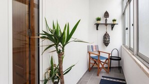 A narrow hallway with a wooden door, a potted plant, a chair, a small table, and a wall-mounted shelf with two plants and a lantern. - Family Apartment with Balcony in Graça (Lisboa)