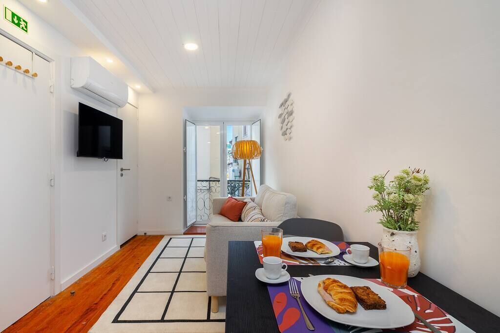 Habitación de hotel con comedor, sofá, televisor y planta.