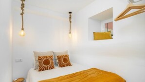 Une chambre à coucher avec un lit, deux luminaires suspendus, une table de chevet et un miroir au mur.