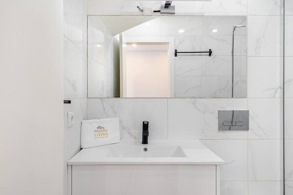 Un baño moderno con lavamanos de mármol blanco, un espejo grande y un perchero para toallas.