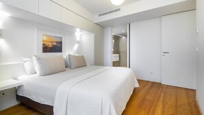 A modern bedroom with a large bed, a nightstand, a wall-mounted light, and a door leading to a bathroom. - City View Penthouse Luxurious Living in Lisbon (Lisboa)