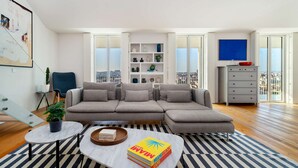Una sala de estar moderna con un sofá modular, una mesa de centro, una estantería y vistas a la ciudad a través de amplios ventanales.