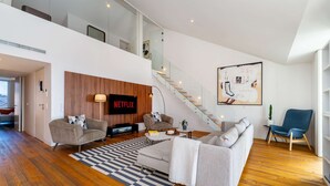 Una sala de estar moderna con un televisor de Netflix, una escalera y un cuadro abstracto grande.
