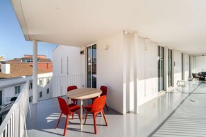 Un balcon avec une table et des chaises, de grandes fenêtres et une vue sur les immeubles.