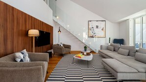 Una sala de estar moderna con una escalera, un televisor de pantalla plana y un gran ventanal.