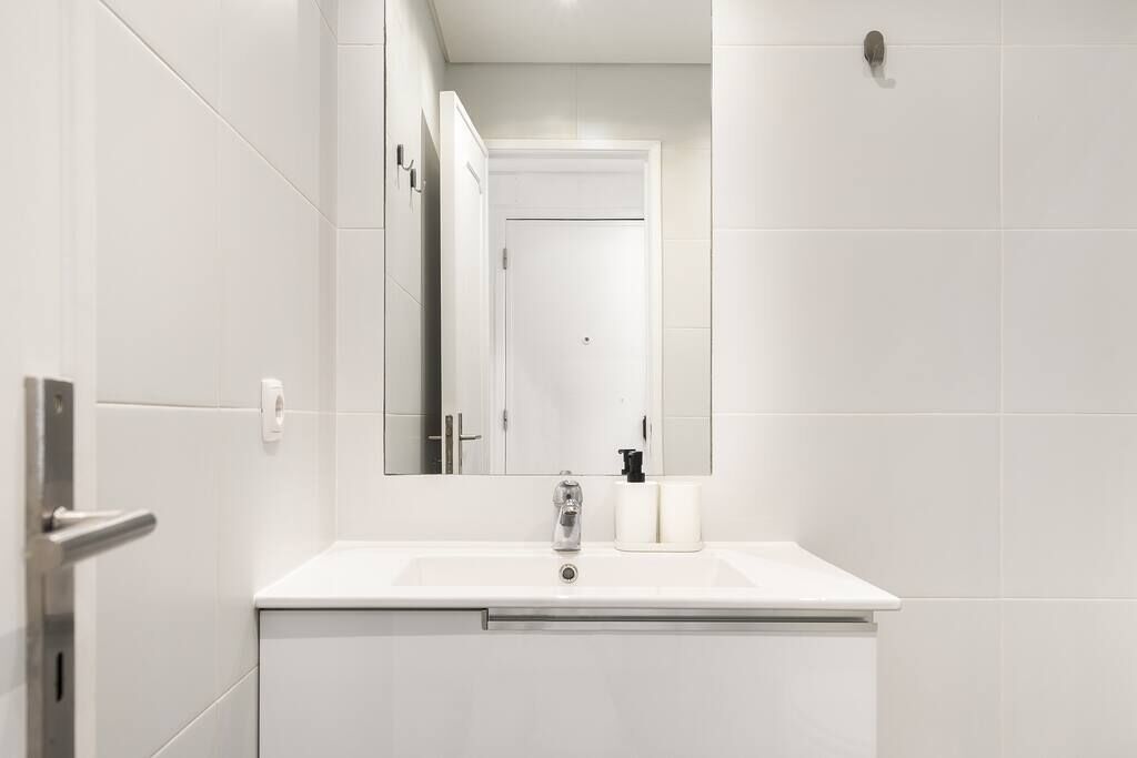 Un baño moderno con azulejos blancos, un lavamanos con grifo, un espejo y un inodoro.