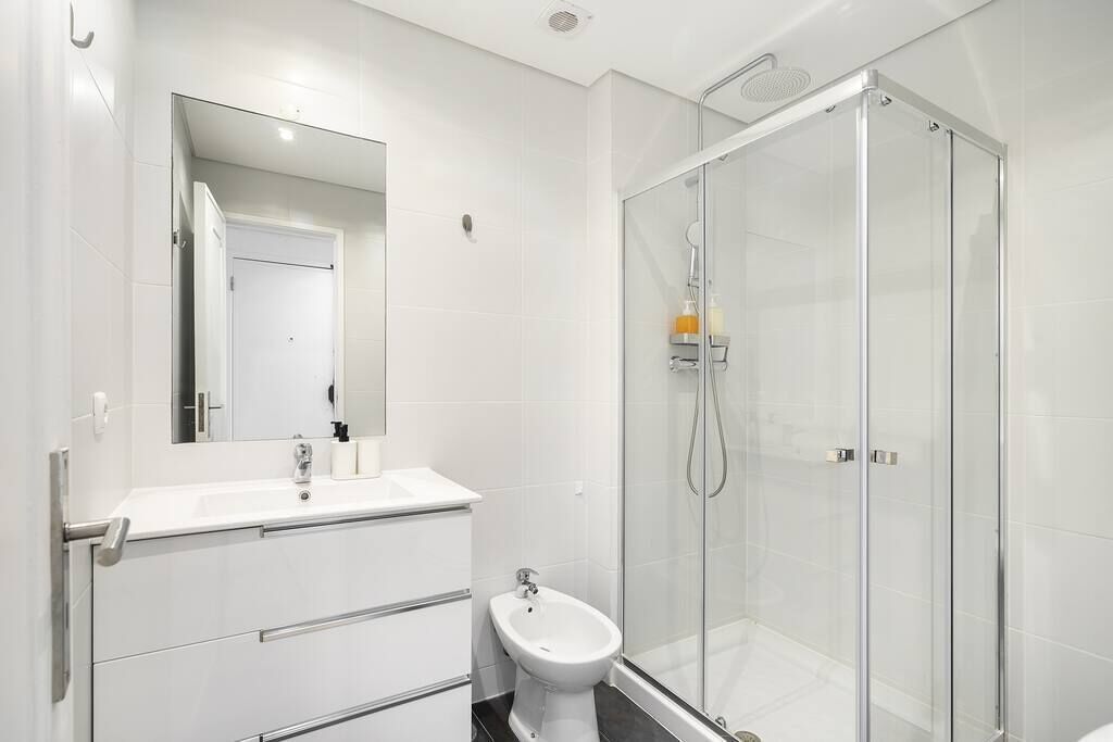 Et moderne badeværelse med en glasvæg omkring brusenichen, en hvid vask og en bidet.