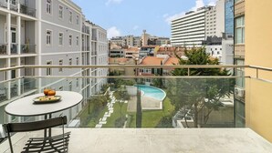 A balcony with a glass railing overlooking a swimming pool and a garden.