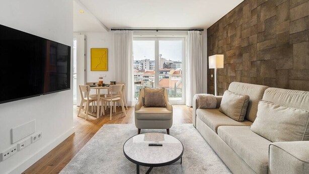 A modern living room with a flat-screen TV, a sofa, a coffee table, and a dining area with chairs and a table.